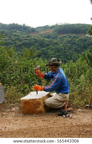 LAM DONG, VIET NAM- NOVEMBER 28: Worker with splitter and hammer on hand try to split large rock into small size for road-works at mountain pass in Lam Dong, Viet Nam in November 28, 2013