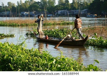 DONG THAP, VIET NAM- NOVEMBER 12: Couple of fisherman catch fish on river in flood season, the woman rowing the row boat, the man do fishing, river cover by water hyacinth in Viet Nam on Nov 12, 2013