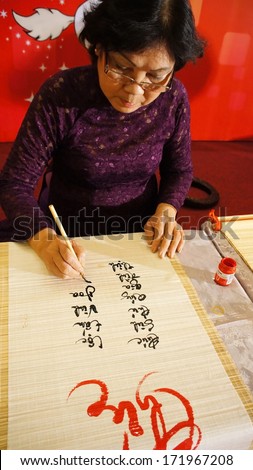 HO CHI MINH CITY, VIET NAM-JAN 15: Woman writing calligraphy, she write vietnamese letter at year end event, calligrapher who have kind face, intellectual wear traditional dress, Vietnam, Jan 15, 2013