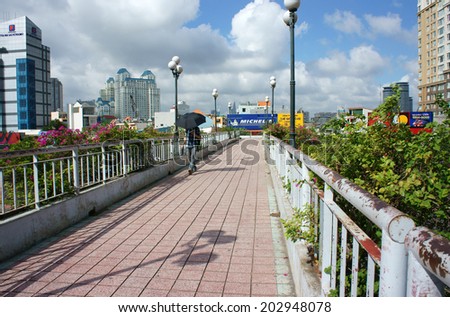 HO CHI MINH CITY, VIETNAM- JULY 3: Young man walking on overpass with umbrella in hand in hot day, he walk alone, cloudy sky, sunshine in summer, Viet Nam, July 3, 2014