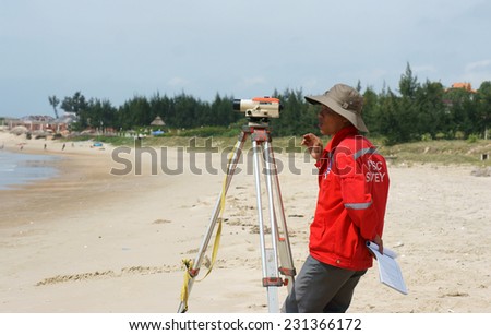 BINH THUAN, VIET NAM- OCT 21: Asian engineer work on Vietnamese beach, man looking in theodolite to survey sea level, measurement device set on tripod, Vietnam, Oct 21, 2013