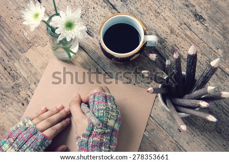 Women hand wear wool gloves in wintertime, writting letter for lover from distant, lonely background in cold day of christmas season, hot coffee cup, flower pot, pencil on wooden background