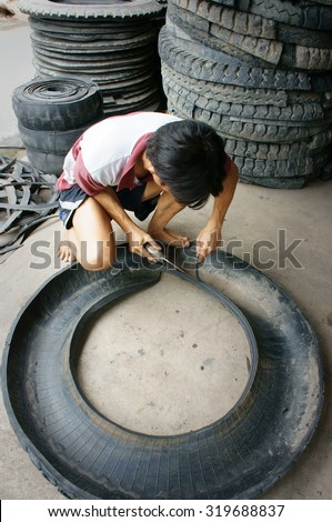 VINH LONG, VIET NAM- JULY 27: Vietnamese worker working at Mekong Delta trade village to recycle tire, man cut out rubber from tyre, Vinhlong, Vietnam, July 27, 2015