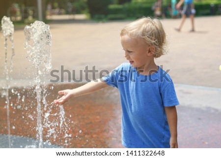 A boy playing with water in park fountain. Hot summer. Happy young boy has fun playing in water fountains 