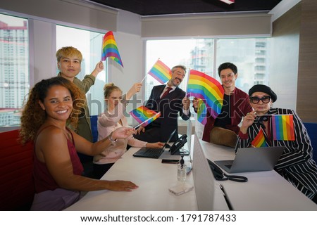 diverse business people (man, woman, gay, transgender, lesbian, asian, caucasian, african american, lgbtq) with rainbow flag on hand in business office working together as teamwork selective focused