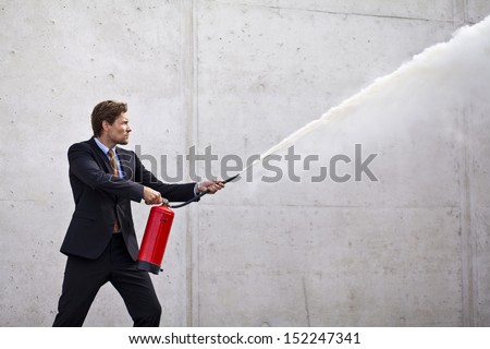Businessman using fire extinguisher at a target as if controlling damage or problems