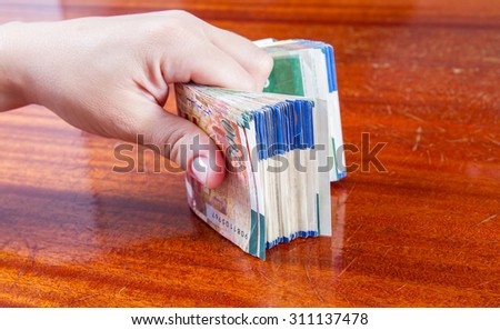 A female hand holding two hundred shekel bank notes against wood background. Concept photo of money, banking ,currency and foreign exchange rates.