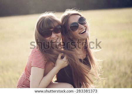 Two young woman making fun on nature at sunset.