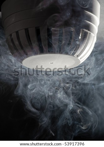 Closeup of a smoke or fire detector with wispy smoke nearby.