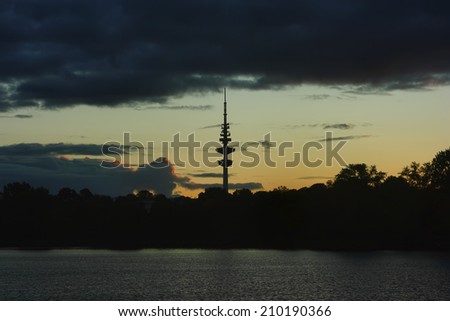 Hamburg TV tower. The water surface of lake and the contour of TV tower of Hamburg against the evening sky with a stripe of clouds and dark outline of the city park.