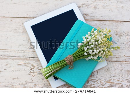 diary, a tablet computerand  lilies of valley on the table