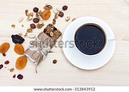 Homemade rustic granola bars with dried fruits and handmade packaged and cup of coffee on wooden background