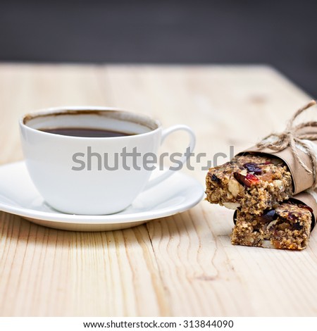 Homemade rustic granola bars with dried fruits and handmade packaged and cup of coffee on wooden background
