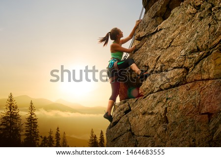 Beautiful Woman Climbing on the High Rock at Foggy Sunset in the Mountains. Adventure and Extreme Sport Concept 商業照片 © 
