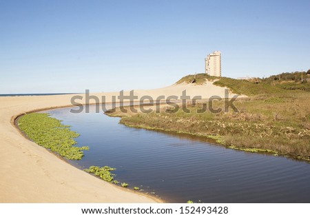 A closed lagoon inlet to the ocean at low tide surrounded by sand dunes and vegetation