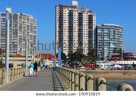 DURBAN; SOUTH AFRICA - MAY 3; 2014: People walk along concrete pier towards commercial and residential buildings on beachfront in Durban South Africa