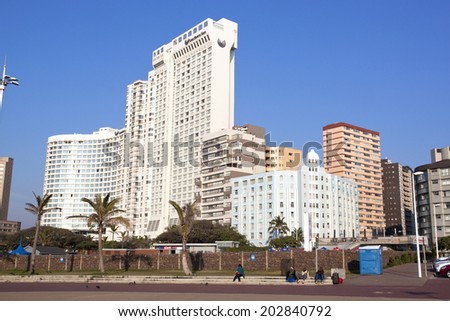 DURBAN, SOUTH AFRICA - JULY 2, 2014: Four unknown people sit on promenade in front of residential and commercial buildings on Golden Mile beach front in Durban, South Africa