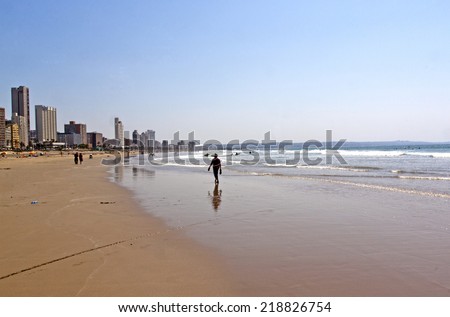 DURBAN, SOUTH AFRICA - SEPTEMBER 21, 2014: Many unknown surfers and people on Addington beach against early morning city skyline in Durban, South Africa
