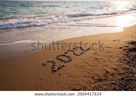 2022 Happy new year concept. Top view of 2022 numbers written on the sand of coastline with wave.Message hand written in golden sand on beautiful sunset or sunrise golden sky background            