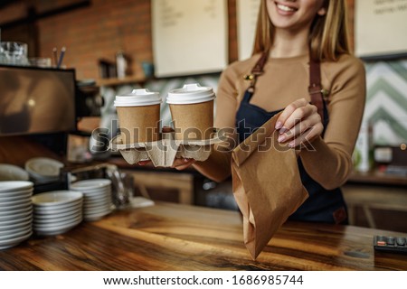Cropped image, barista is working in coffee shop, young woman is standing behind the bar counter, making coffee, take away.