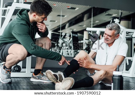In the photo, two people in the gym, one of them on the floor with an injured leg, a rehabilitation coach helps him. Photo stock © 