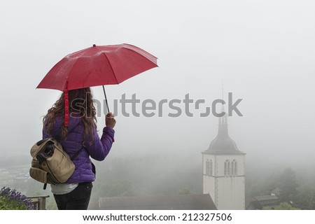 Young woman with red umbrella looking at Gruyere\'s Church, Switzerland, on a misty day