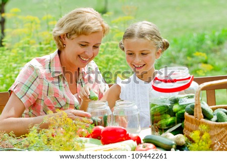 Preparing preserves of pickled cucumbers - girl is helping mother to make preparations of vegetables