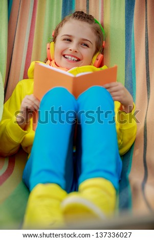 Young girl with book enjoying music. Girl with a book resting on a hammock