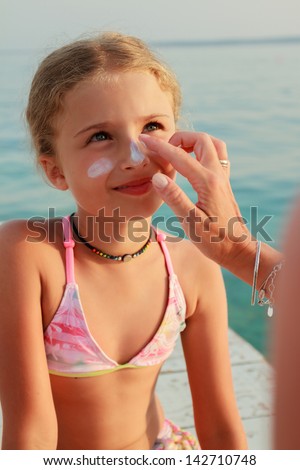 Sun protection. Mother anoints her daughter face protective cream on the beach