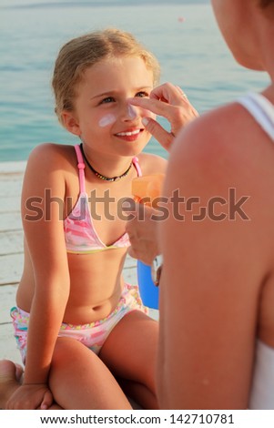 Sun protection. Mother anoints her daughter face protective cream on the beach