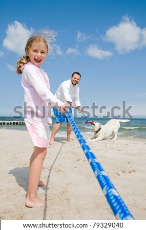 Tug of war - family with dog playing on the beach
