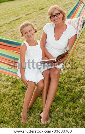 Happy childhood - girl with mother reading a book in colorful hammock
