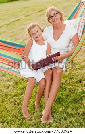 Rest in the garden, happy childhood - girl with mother reading a book in colorful hammock