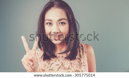 Victory hand sign. Vintage, retro style of portrait of Asian woman in pink vintage dress on blue and green background.