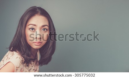 Alarmed face. Vintage, retro style of portrait of Asian woman in pink vintage dress on blue - green background.