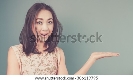 Happy woman is resenting an empty content. Vintage, retro style of portrait of Asian woman in pink vintage dress on blue and green background.