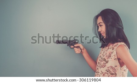 Pointing a gun. Vintage, retro style of portrait of Asian woman in pink vintage dress on blue - green background.