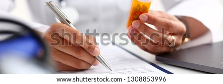 Female black medicine doctor hand hold jar of pills and write prescription to patient at worktable. Panacea and life save, prescribing treatment legal drug store concept. Empty form ready to be used Imagine de stoc © 