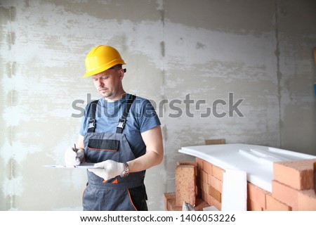 Male builder in yellow hard hat holds clipboard on background of an apartment under repair portrait. Estimated property value concept. Foto d'archivio © 