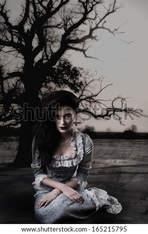 Weird female witch on background with dead tree