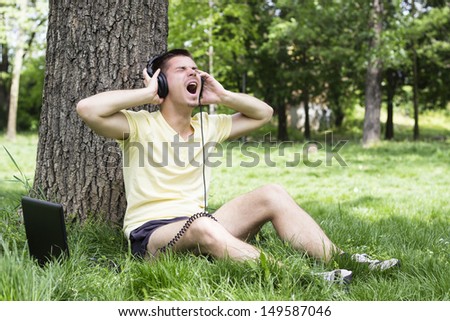 Young man listening music and singing, in the park, spring/summer