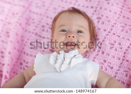 Sweet little baby girl lying on her back wearing a white jacket, looking at the camera and laughing  back.