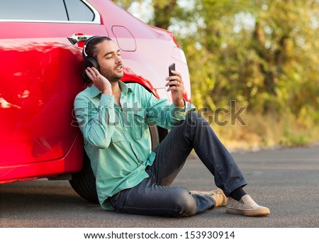 guy listening to music while sitting beside the car on the road