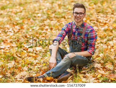 hipster guy sitting in the autumn park smiling