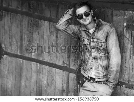 handsome guy with glasses and a fashionable hairdo. vintage photo. The guy standing near the old wall