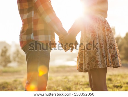 Photo of Young couple in love walking in the autumn park holding hands looking in the sunset