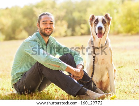 Man and central Asian shepherd walk in the park. He keeps the dog on the leash.