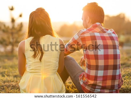 back view of young happy couple sitting on river at sunset