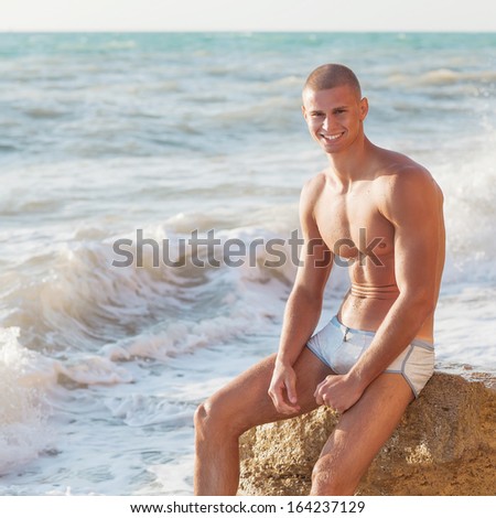 Portrait of a handsome young muscular man in swimtrunks with water ocean background
