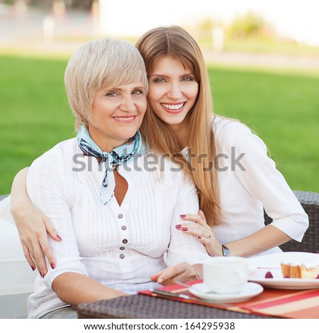 adult mother and daughter drinking tea or coffee and talking outdoors. Mothers day.